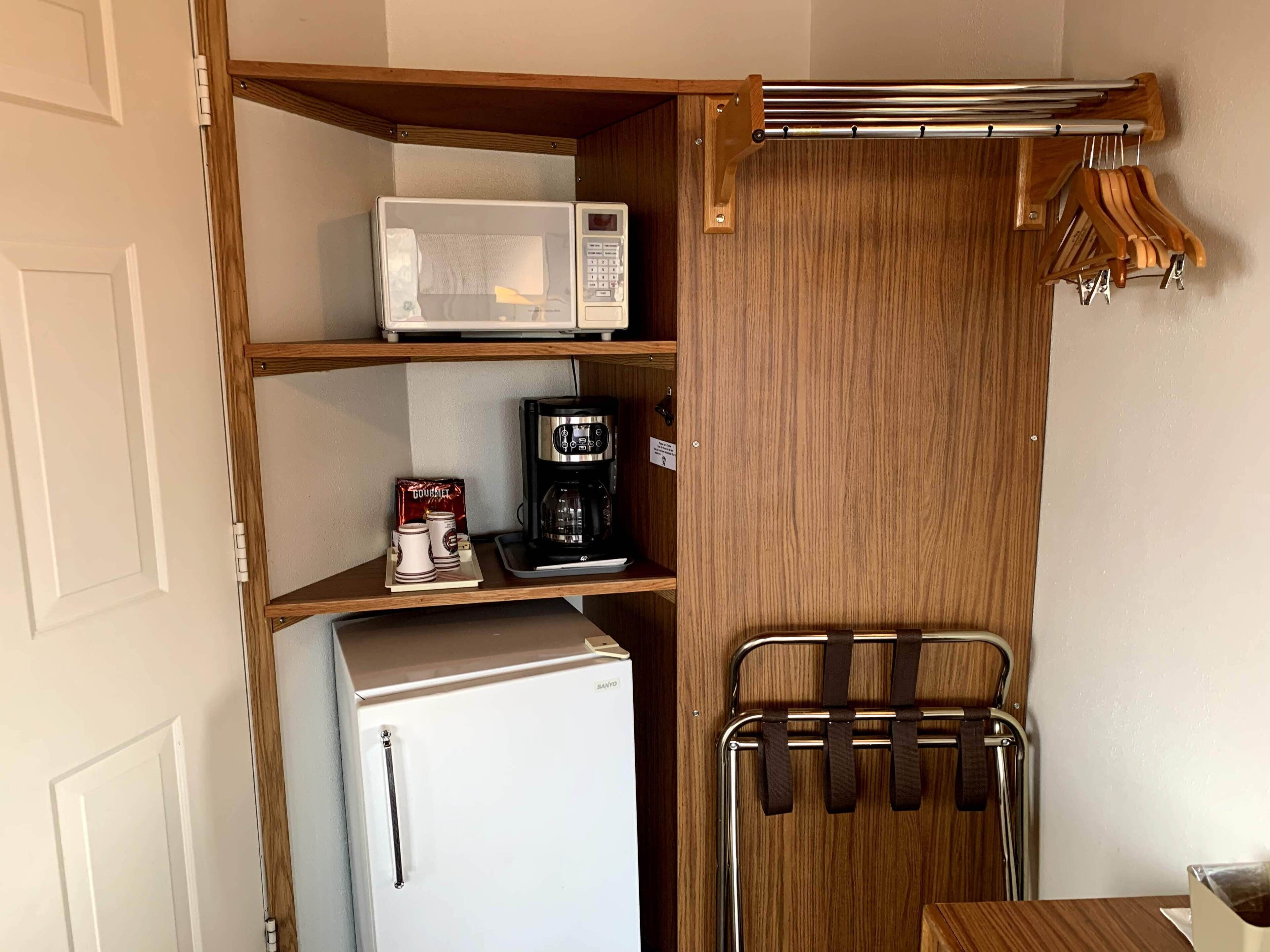Una kitchenette compacta con un refrigerador blanco, un microondas y una cafetera en los estantes.