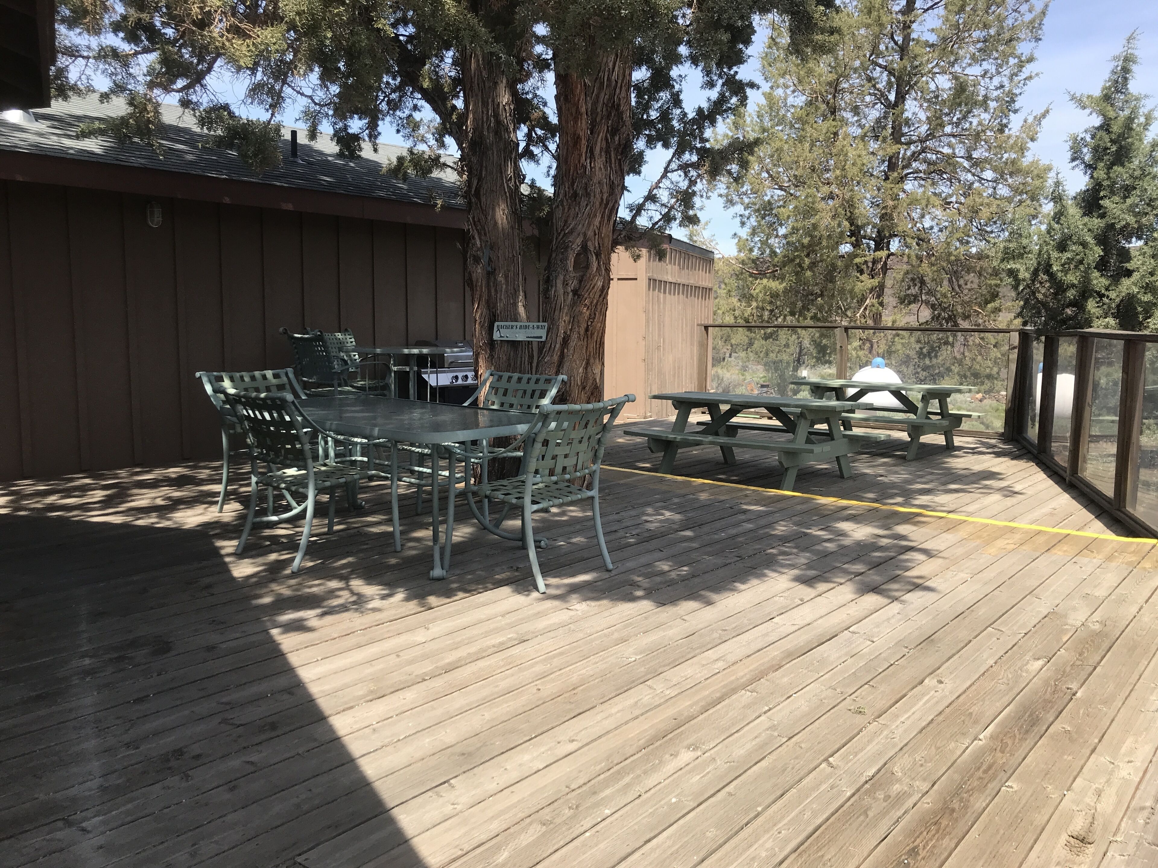 A wooden deck with picnic tables and chairs, a grill, and a sign indicating a private area.