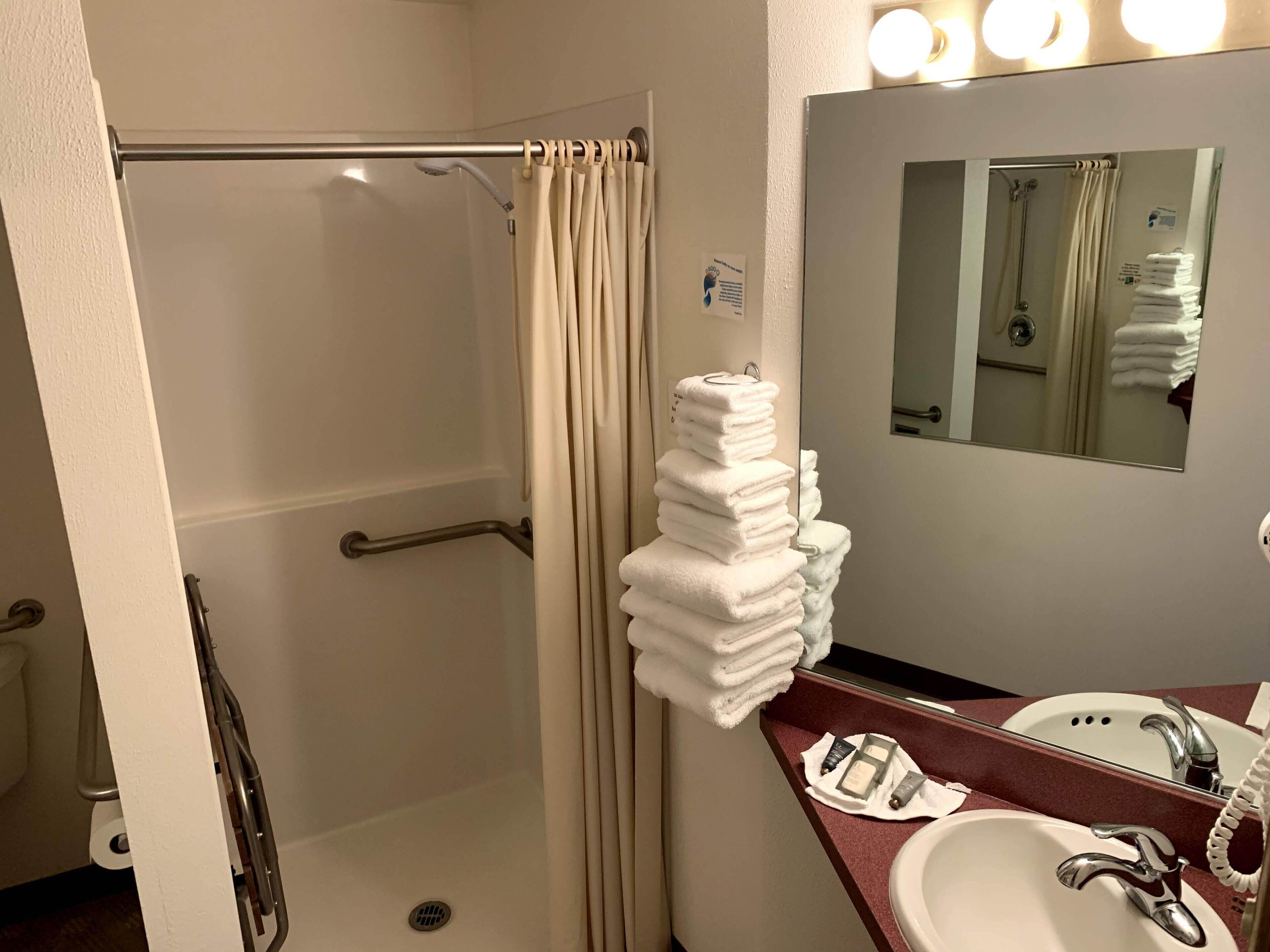Un bagno con doccia, una pila di asciugamani bianchi, un lavandino e uno specchio.