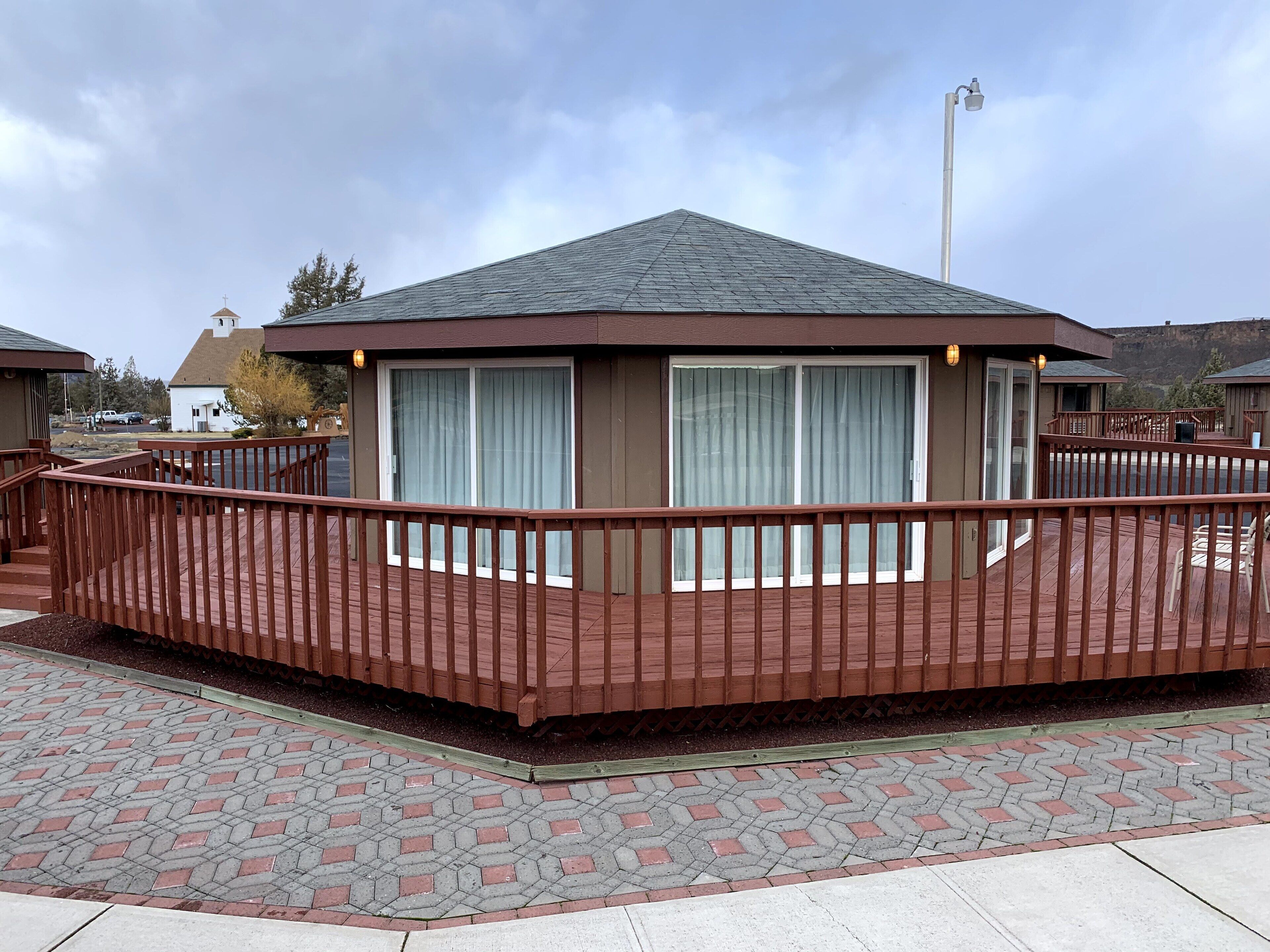 A wooden deck with a railing, a building with a large window, and a cloudy sky.