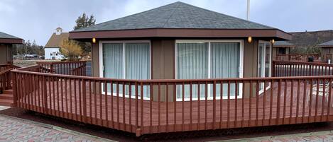 Eine Holzdielen-Terrasse mit Geländer, ein Gebäude mit großem Fenster und ein bewölkter Himmel.