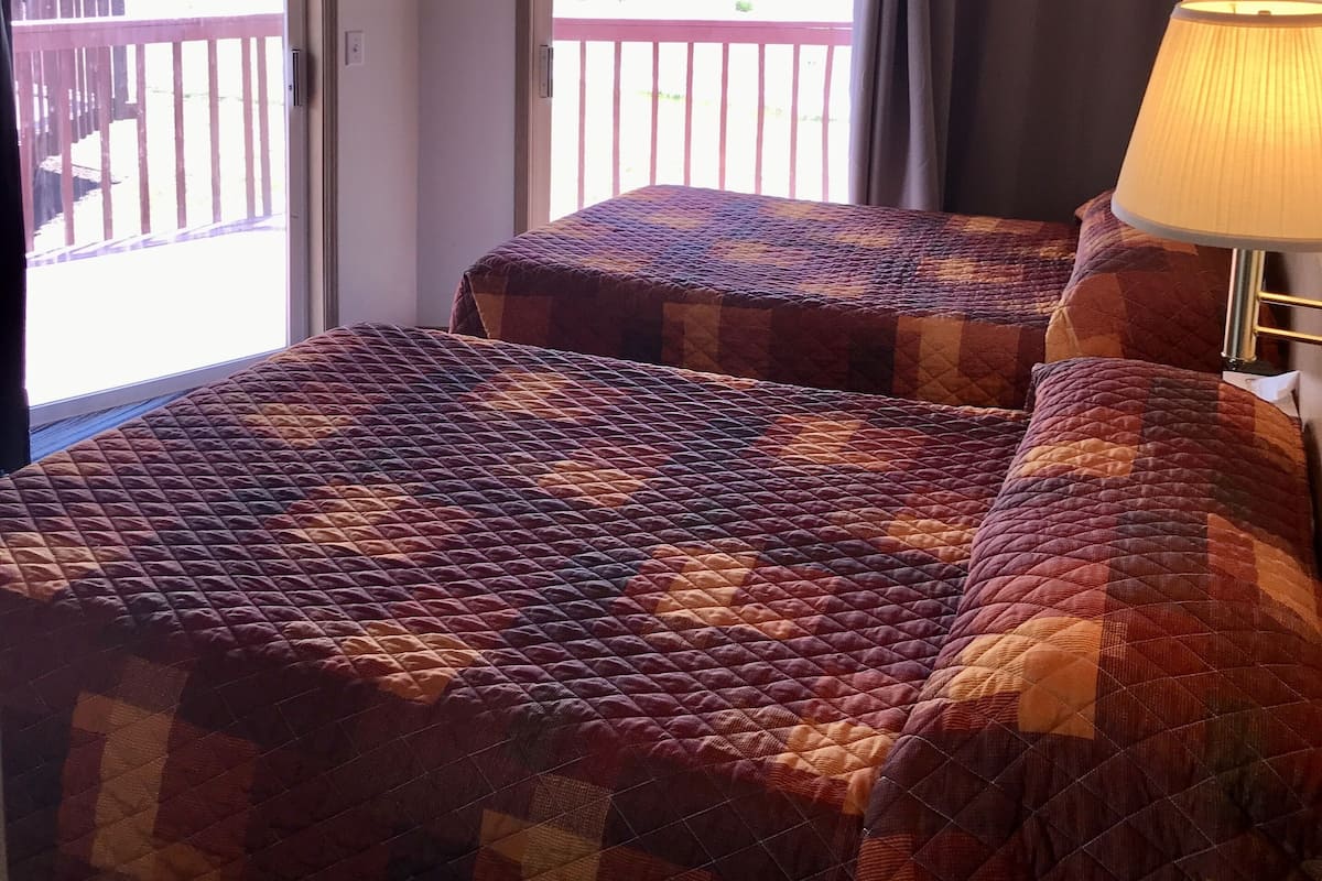 A room with two beds, a wooden ceiling, and a view through a door to an outdoor deck.