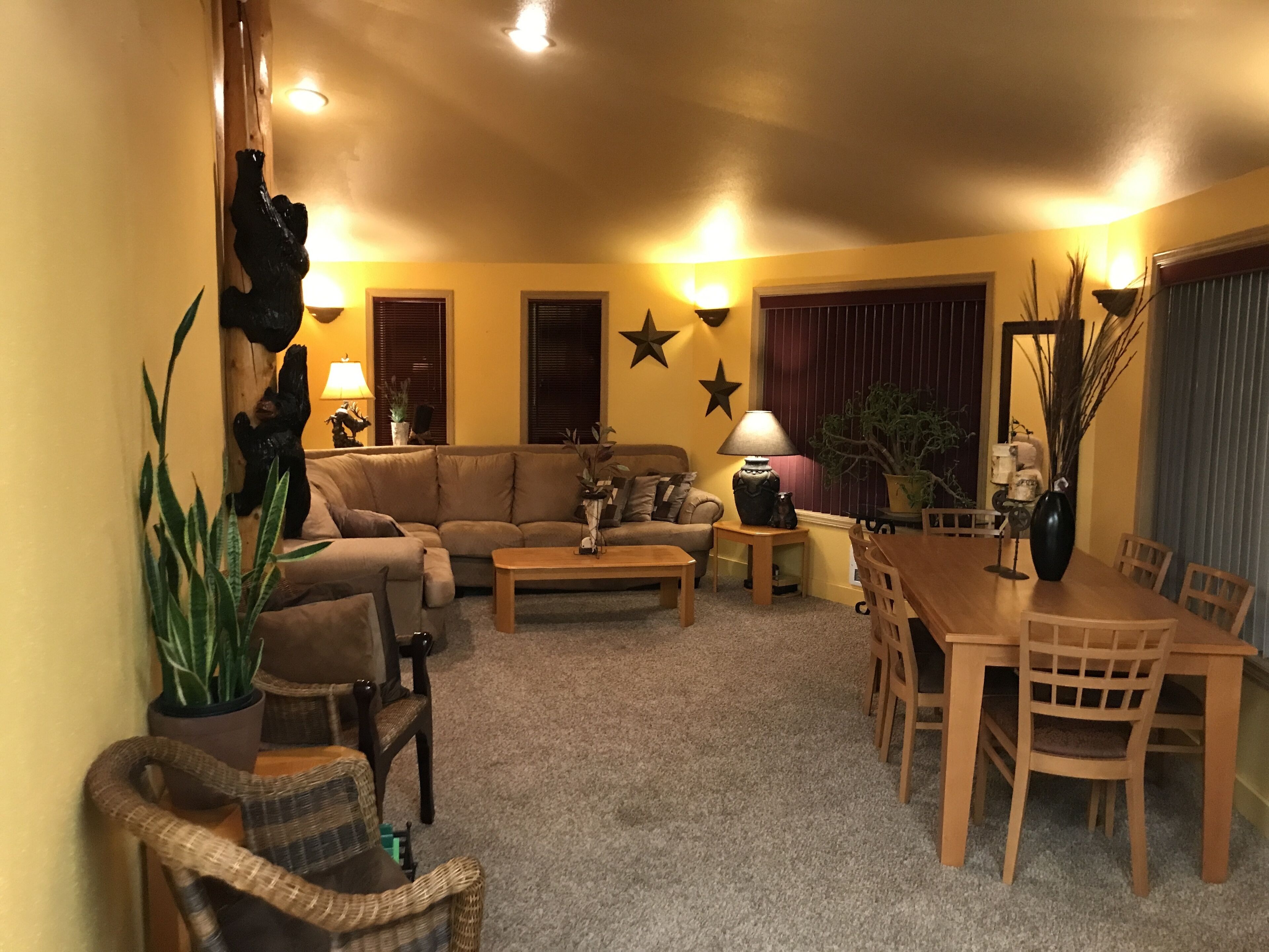 Ein gemütliches Wohnzimmer mit einer Couch, Sesseln, einem Couchtisch und einem Esstisch mit Stühlen. An den Wänden sind dekorative Sterne, und auf einem Beistelltisch steht eine Lampe.