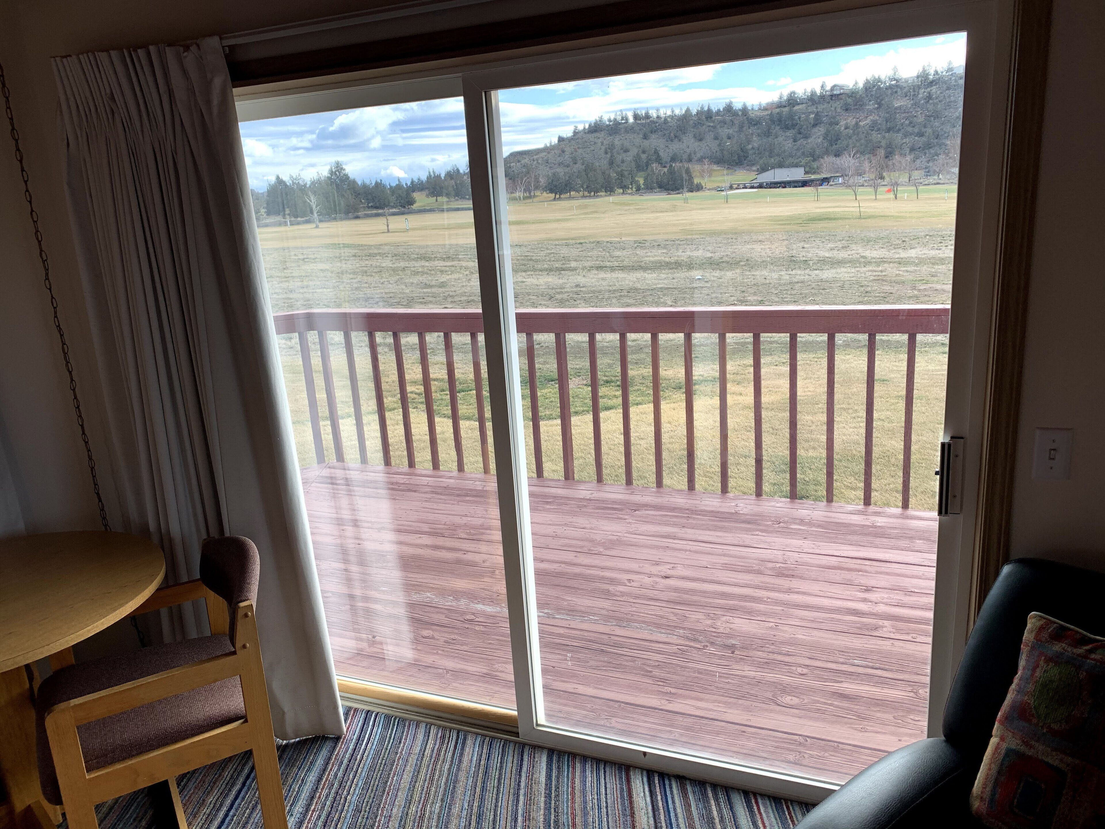 A room with a wooden chair, a small table, and a view through a sliding glass door to a deck with a red railing.