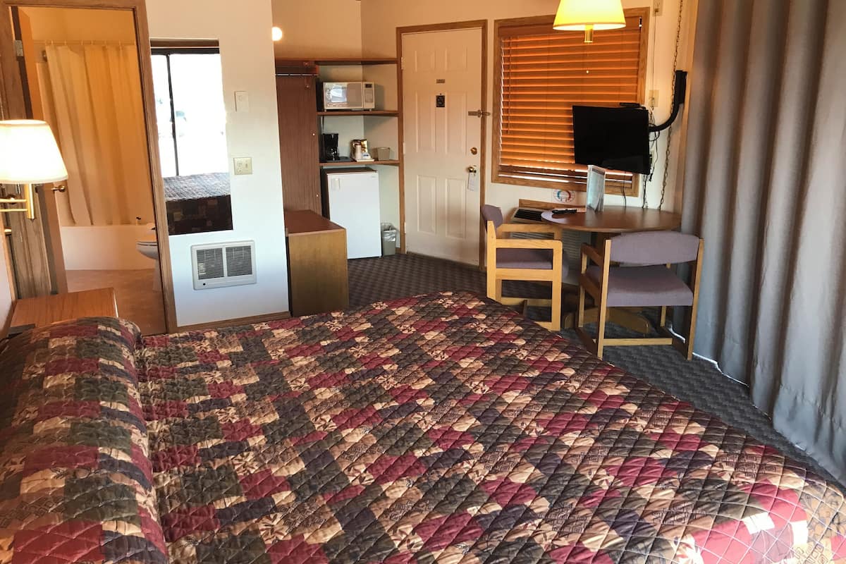 A compact room with a bed, a desk, a chair, and a kitchenette.