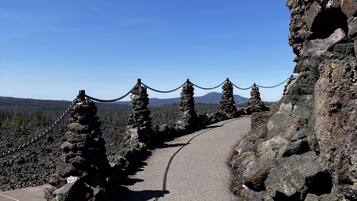 Un sendero pavimentado con una cerca de malla metálica, rodeado de terreno rocoso y vegetación escasa.