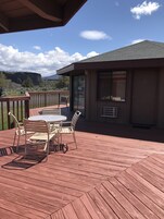 Una terraza de madera con una mesa y sillas, con vistas a un paisaje montañoso.