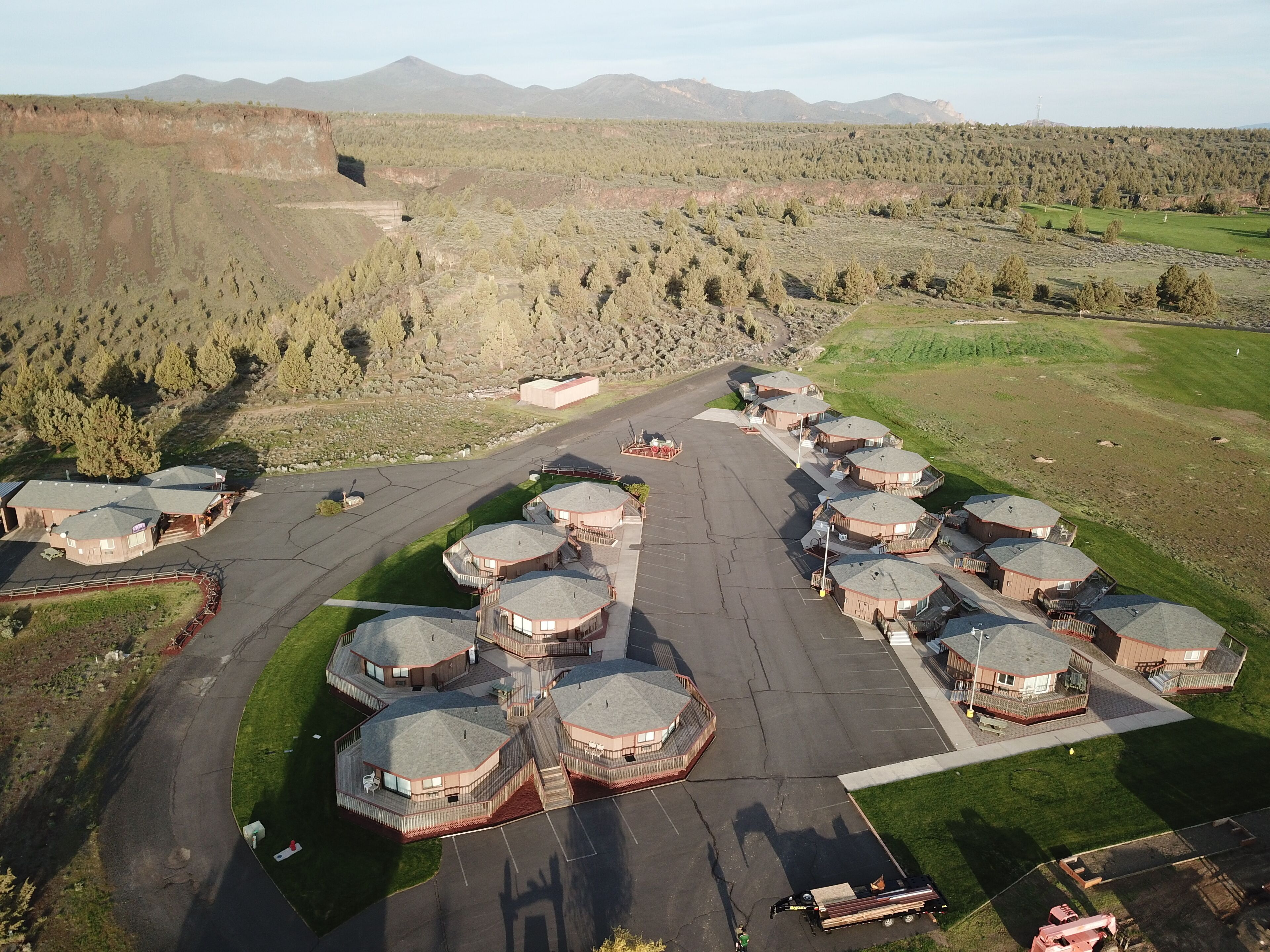 An aerial view of a resort with multiple hexagonal buildings, a parking area, and a mountainous backdrop.