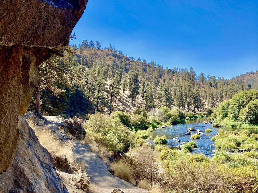 Un paisaje natural con un río, terreno rocoso y un cielo azul despejado.