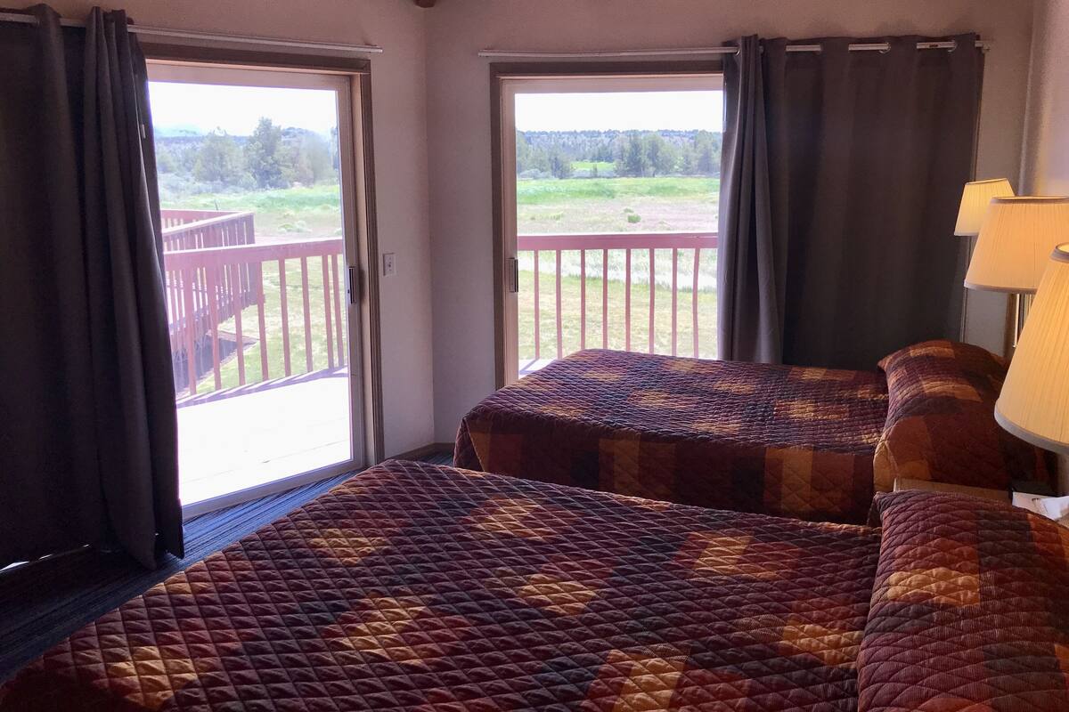 A room with two beds, a balcony with a wooden railing, and a lamp.