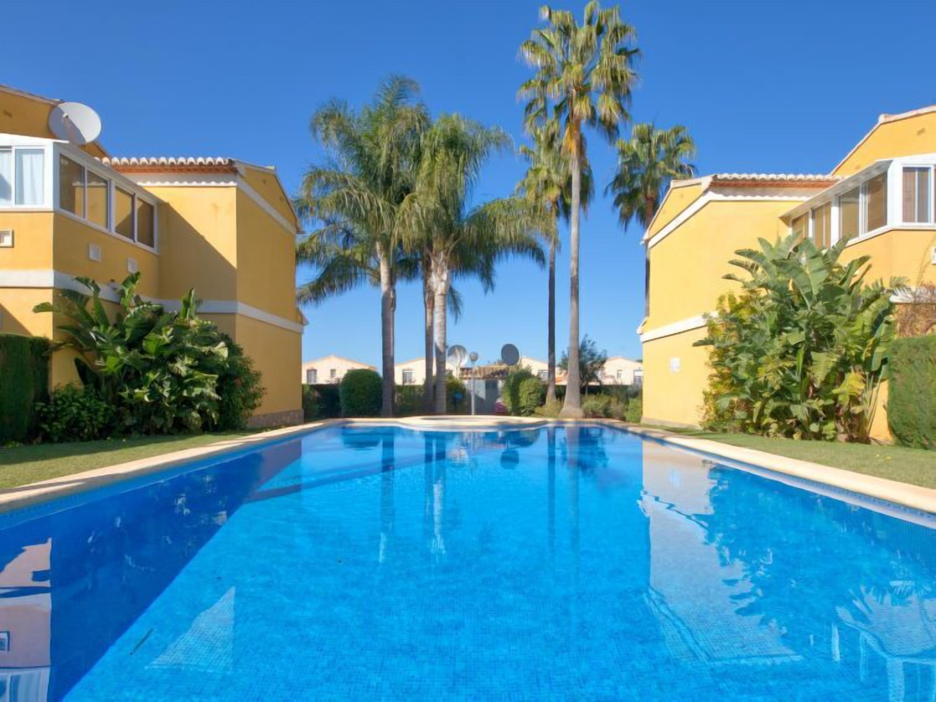 Ein Swimmingpool, umgeben von gelben Gebäuden mit Palmen.