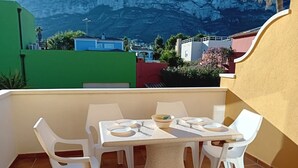 A terrace with a table set for four, surrounded by white plastic chairs, overlooking a coastal town with buildings and a mountain in the background. - Alqueria Sol by Interhome (Dénia)