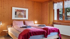 A wooden-paneled bedroom with a bed, a framed abstract painting, and a window with curtains.