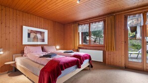 A wooden-paneled bedroom with a bed, a window with curtains, and a radiator.
