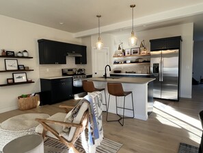 A modern kitchen with dark cabinets, a stainless steel refrigerator, and a central island with bar stools. - Newly Renovated: Experience Redmond Charm near Deschutes + Sunsets (Redmond)