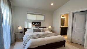 Ein Schlafzimmer mit einem großen Bett, Nachttischlampen, einem Fenster mit Vorhängen, einem Spiegel und einer Tür zu einem Badezimmer.