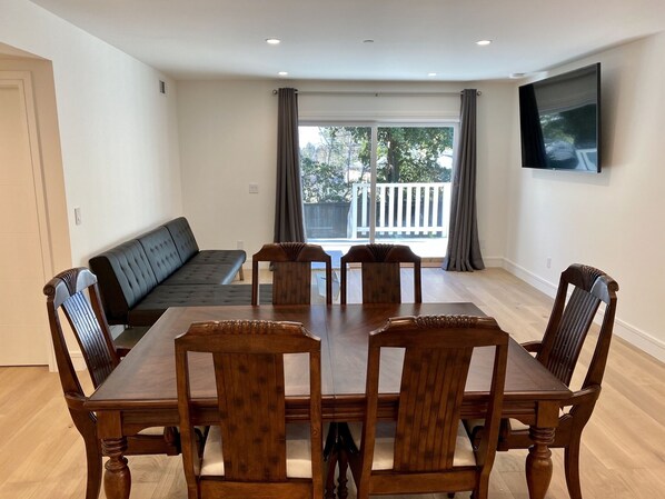 Un coin repas avec une table et des chaises en bois, un canapé noir et un téléviseur fixé au mur.