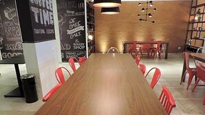 A long wooden table with red chairs in a modern interior with a brick wall and hanging lights. - Ramada Encore Centro (São Paulo)