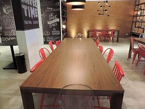 Une longue table en bois, entourée de chaises rouges, dans un intérieur moderne avec un mur en briques et des luminaires suspendus.