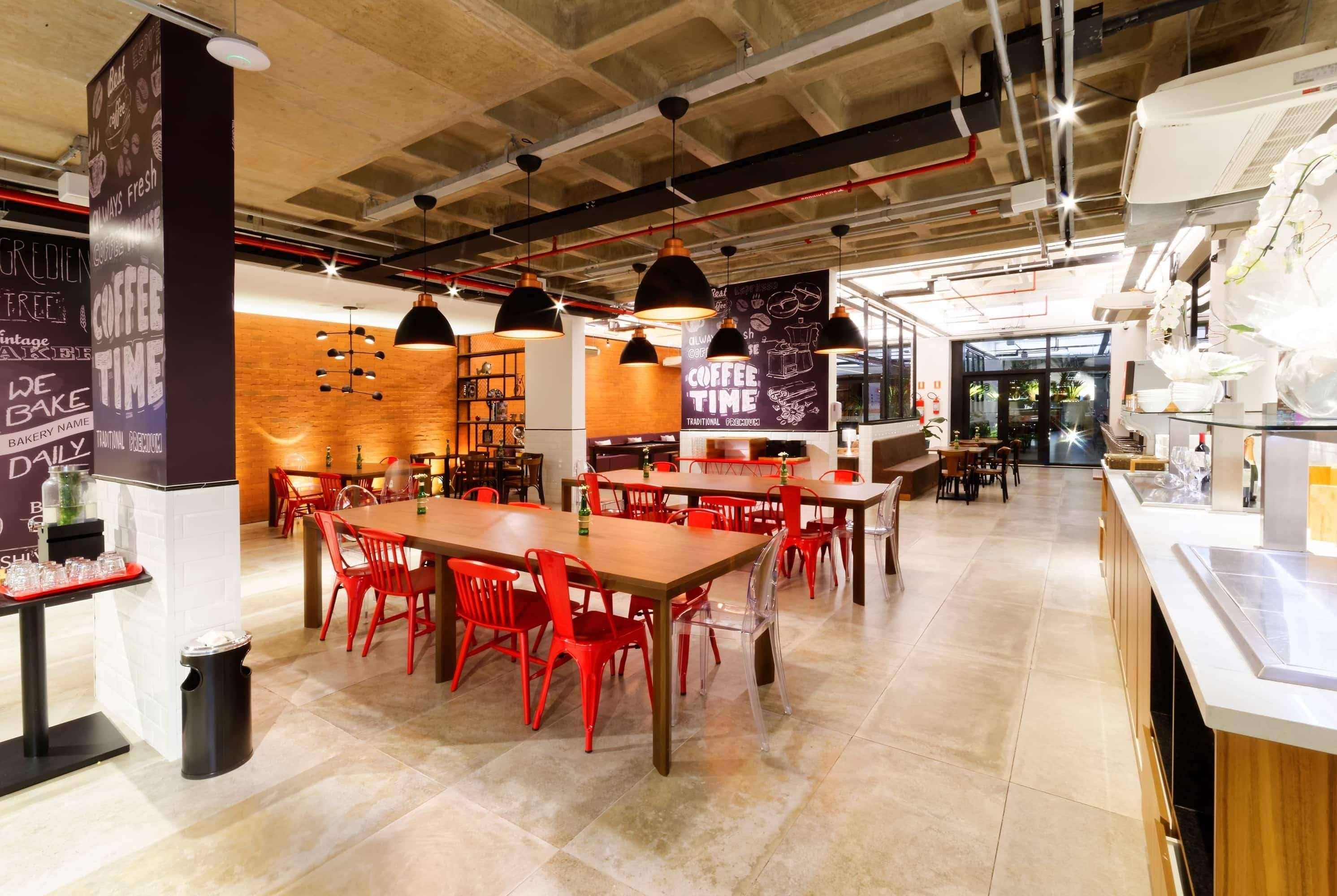 A modern cafe interior with exposed ceilings, red chairs, and black pendant lights.
