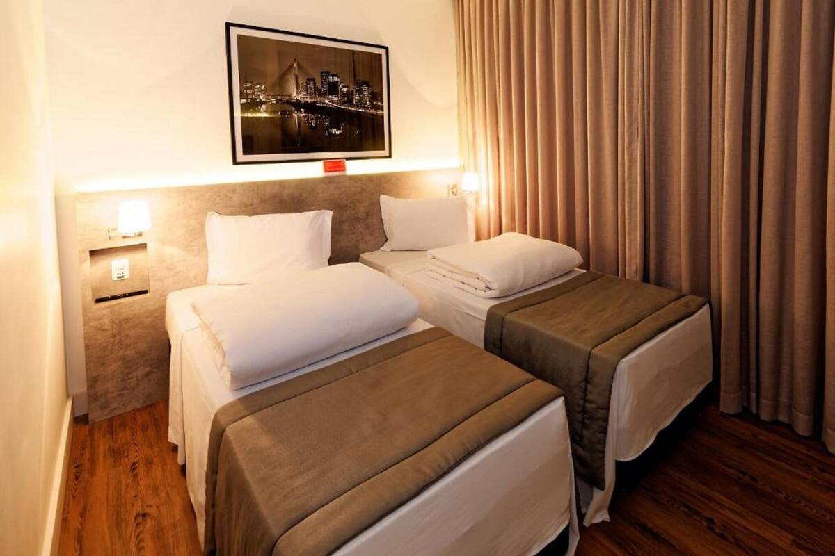 A hotel room with two beds, a cityscape view, and a curtain on the window.