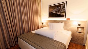 A hotel room with a neatly made bed, a cityscape picture on the wall, and a wooden floor. - Ramada Encore Centro (São Paulo)