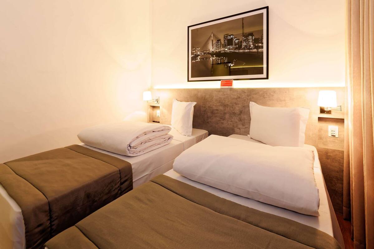 A hotel room with two beds, a large framed picture on the wall, and bedside lamps.