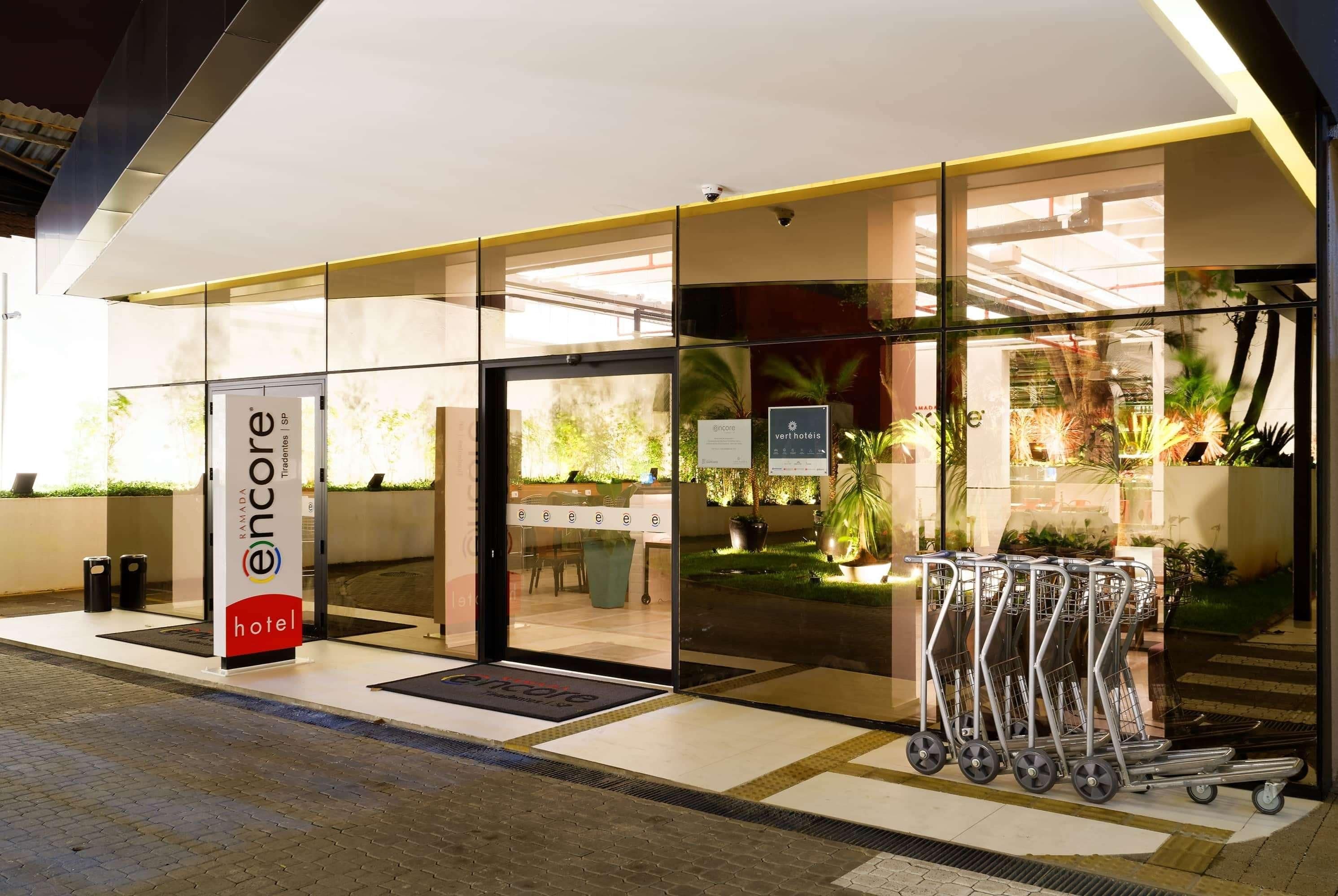 Entrada moderna de hotel com portas de vidro, balcão de recepção e placa com a inscrição 'Encore Hotel'.
