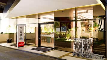 Entrada moderna de hotel com portas de vidro, balcão de recepção e placa com a inscrição 'Encore Hotel'.