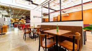 A modern cafe interior with wooden tables and chairs, a visible 'encore' sign, and a brick wall in the background. - Ramada Encore Centro (São Paulo)