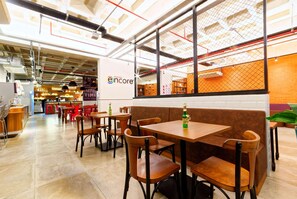 L’intérieur d’un café moderne, avec des tables et des chaises en bois, un panneau indiquant « Encore » bien visible, et un mur de briques en arrière-plan.