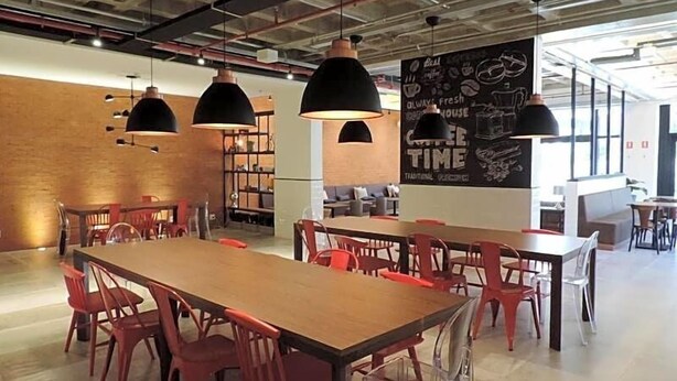 A modern cafe with wooden tables and red chairs, black pendant lights, and a chalkboard menu. - Ramada Encore Centro (São Paulo)