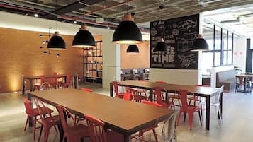 Um café moderno com mesas de madeira e cadeiras vermelhas, luminárias pendentes pretas e um menu em lousa.