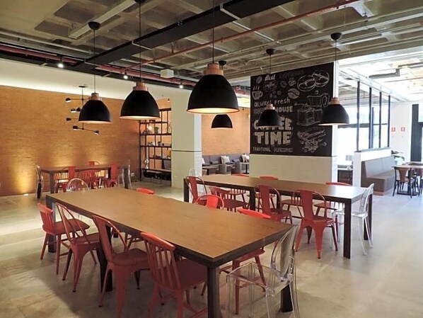 Un café moderne avec des tables en bois et des chaises rouges, des suspensions noires et un menu écrit à la craie sur un tableau noir.