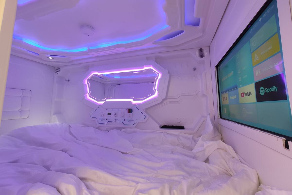 Ein futuristisches Schlafzimmer mit Bedienfeld, einem Bett und einem Bildschirm, der verschiedene Anwendungen anzeigt.