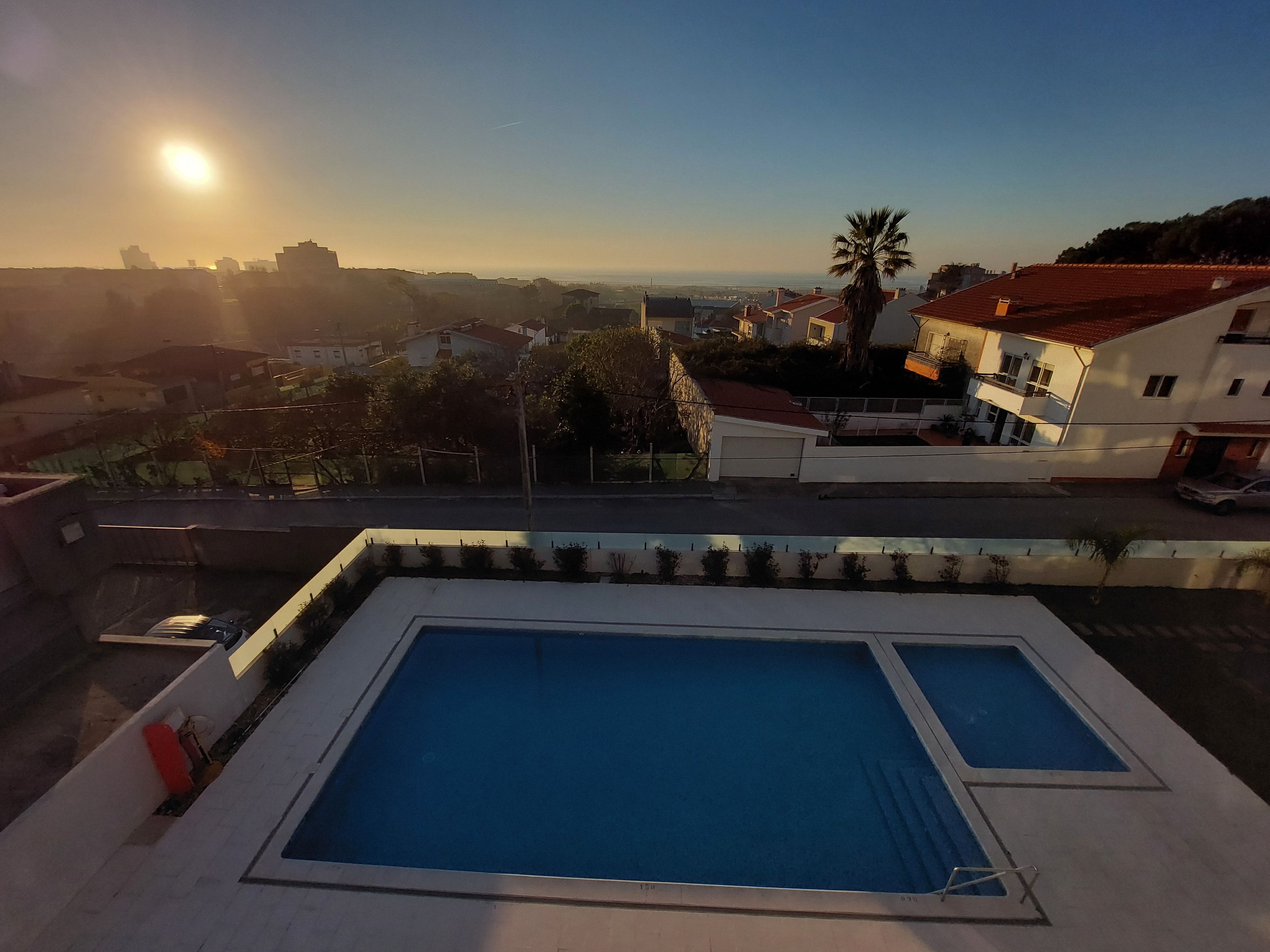 Piscina no terraço com vista clara do bairro ao redor e um pôr do sol ao fundo.
