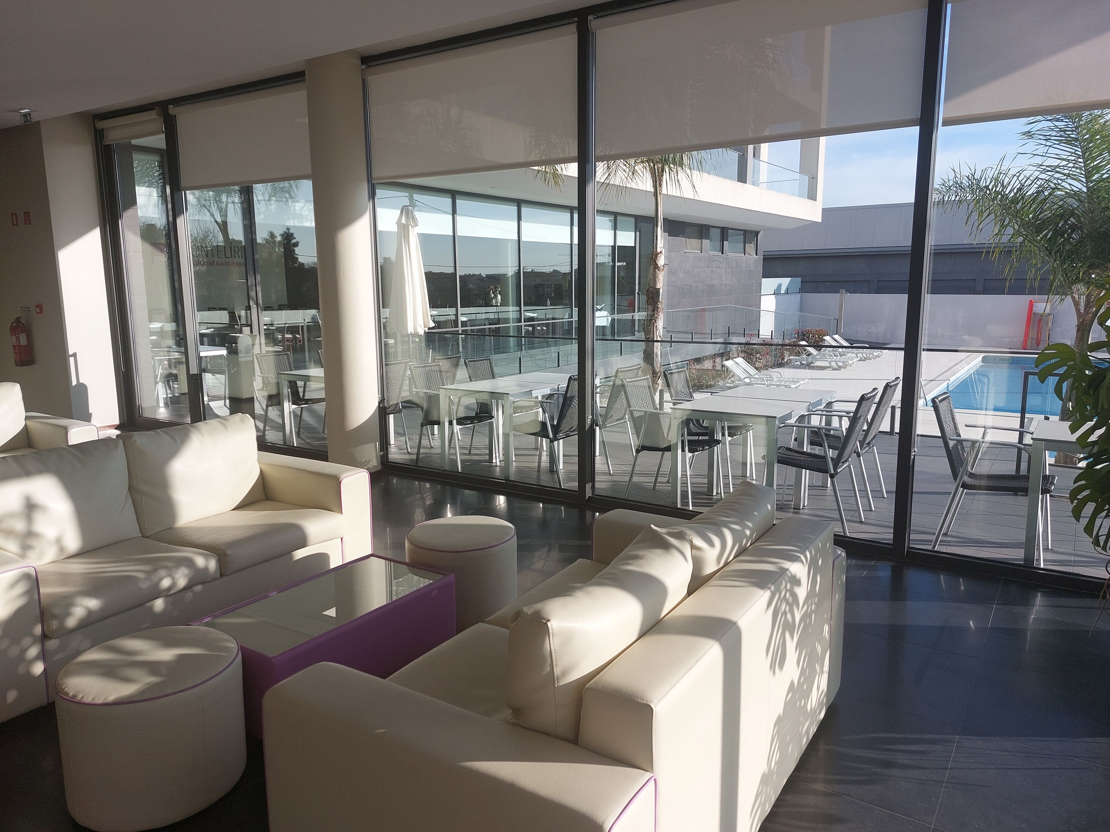 Um hall de hotel moderno com grandes janelas, área de piscina e assentos externos.