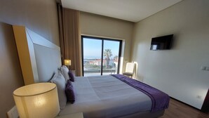 Ein Hotelzimmer mit Bett, Schreibtisch mit Lampe, Wandfernseher und Blick auf die Stadt durch das Fenster.