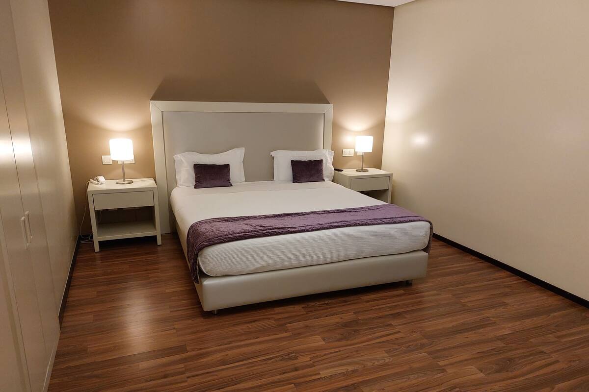 Un dormitorio con una cama, dos mesitas de noche y suelo de madera.