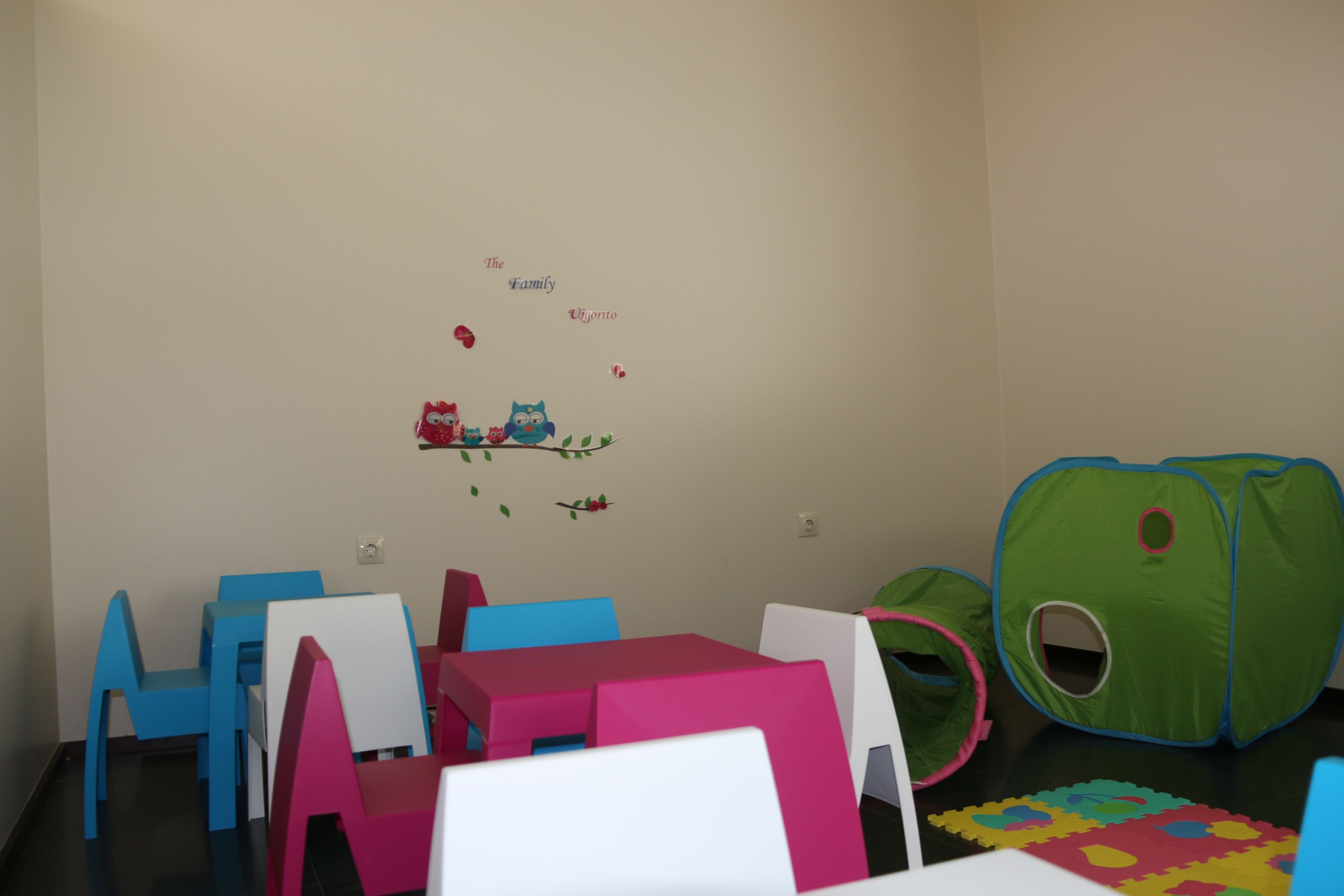 Una sala de juegos para niños con sillas de colores, un corralito verde y un adhesivo de pared.