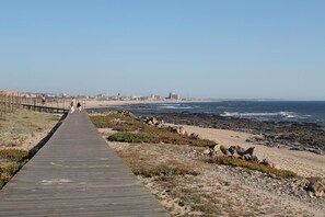 A wooden boardwalk leading to a beach with rocky terrain and a distant cityscape.