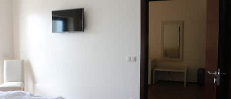 Un dormitorio con cama, televisor montado en la pared y puerta que da a un baño.