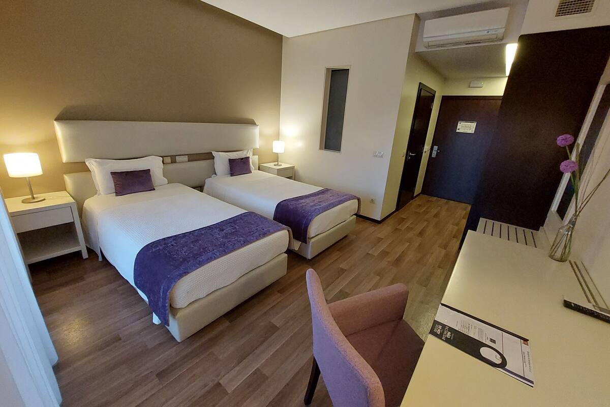 Habitación de hotel con dos camas, un escritorio, una silla y un equipo de aire acondicionado.