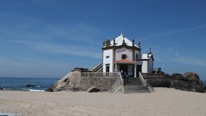 Ein Küstengebäude mit einer Treppe, die zu einer Tür führt, an einem Sandstrand mit großen Felsen in der Nähe.