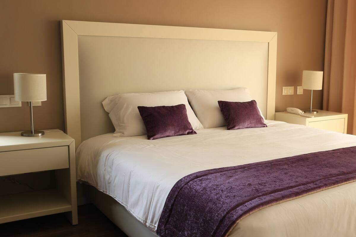 Habitación de hotel con una cama grande, dos mesitas de noche, un teléfono y una lámpara a cada lado.