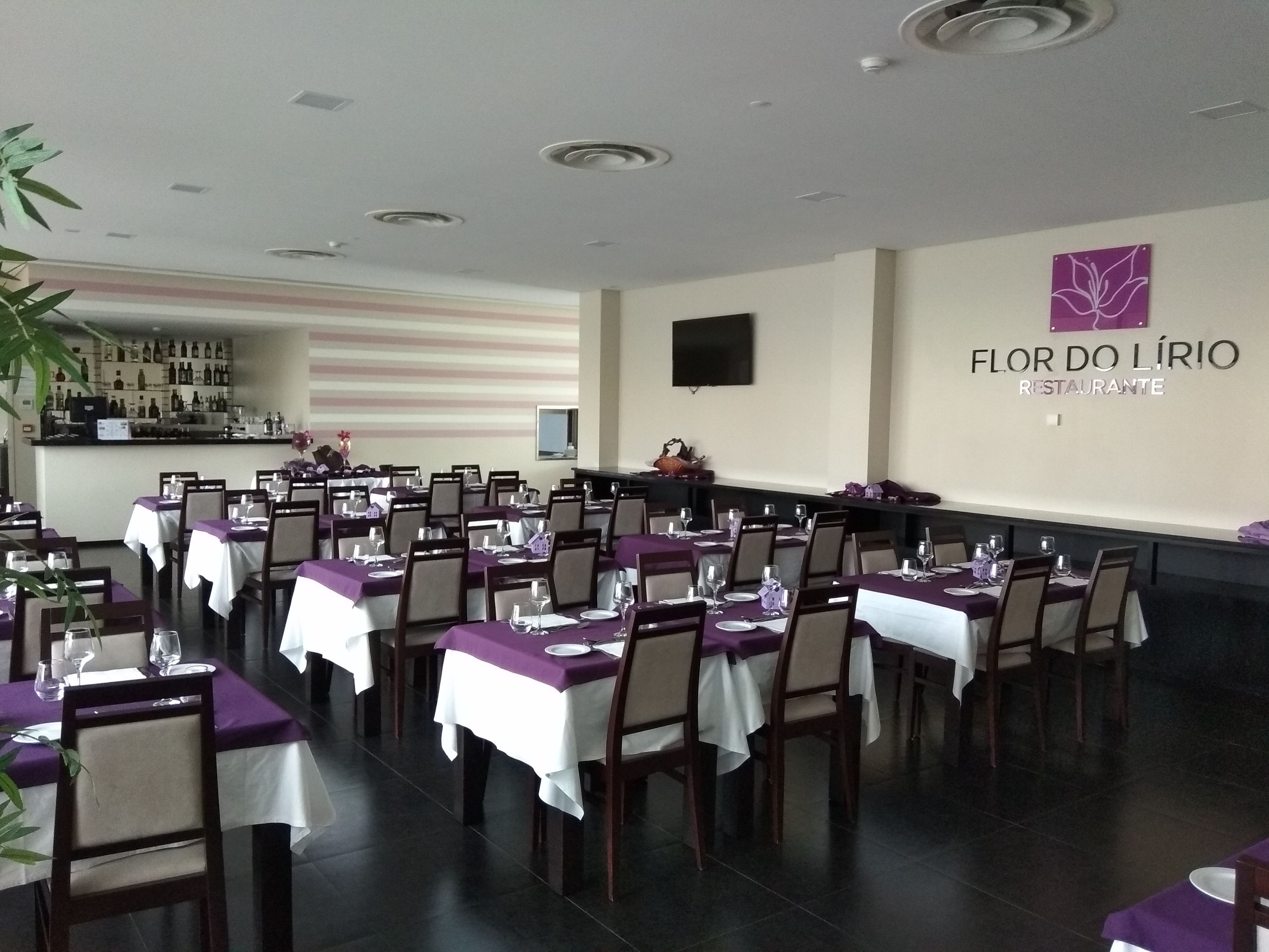 Un interior de restaurante con mesas listas para comer, una zona de bar y un televisor montado en la pared.