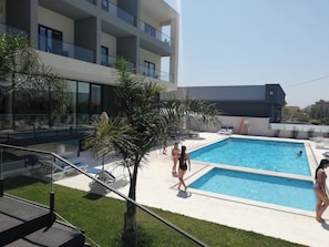 A modern building with a swimming pool, outdoor seating, and palm trees. - Hotel Monte Lírio (Espinho)