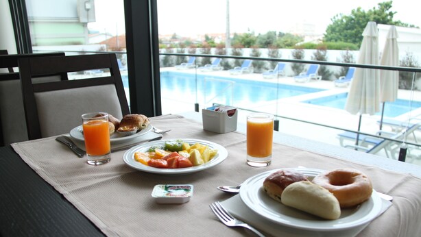 Ein Frühstückstisch mit Speisen, einer Obstschale und Orangensaftgläsern, mit Blick auf einen Swimmingpool.