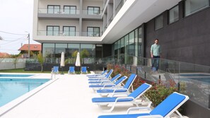 A modern building with a pool area featuring sun loungers and umbrellas. - Hotel Monte Lírio (Espinho)