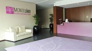 A hotel reception area with a reception desk, a white sofa, and two large potted plants. - Hotel Monte Lírio (Espinho)